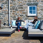 dwy ddynes yn yfed gwin ar soffa braf tu allan